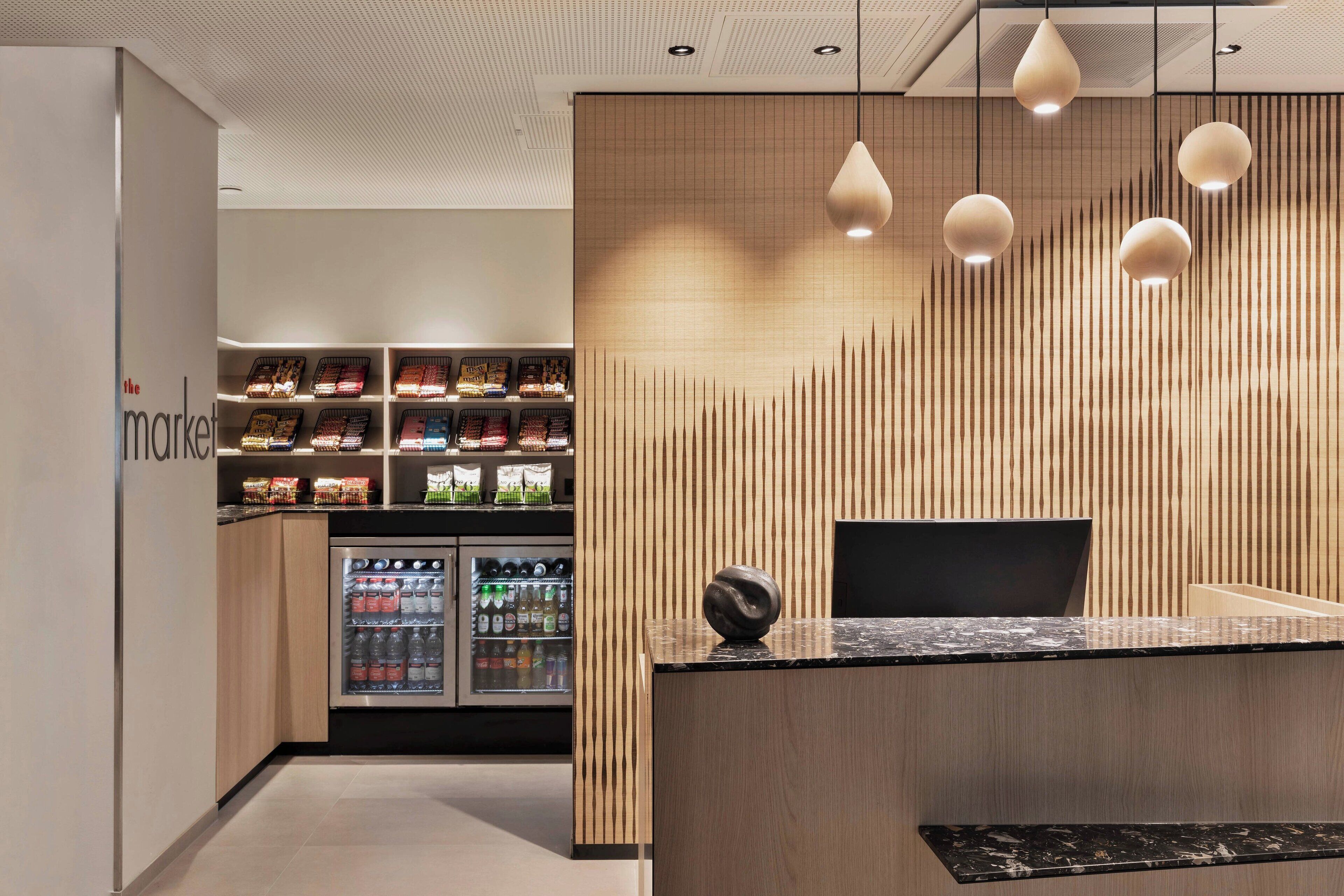 A modern reception area with a wooden accent wall, a black reception desk, and a refrigerated display case with beverages.