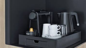 Eine Kaffeemaschine in Schwarz, zwei weiße Tassen, ein Glas und ein kleiner Behälter auf einer schwarzen Tablett.