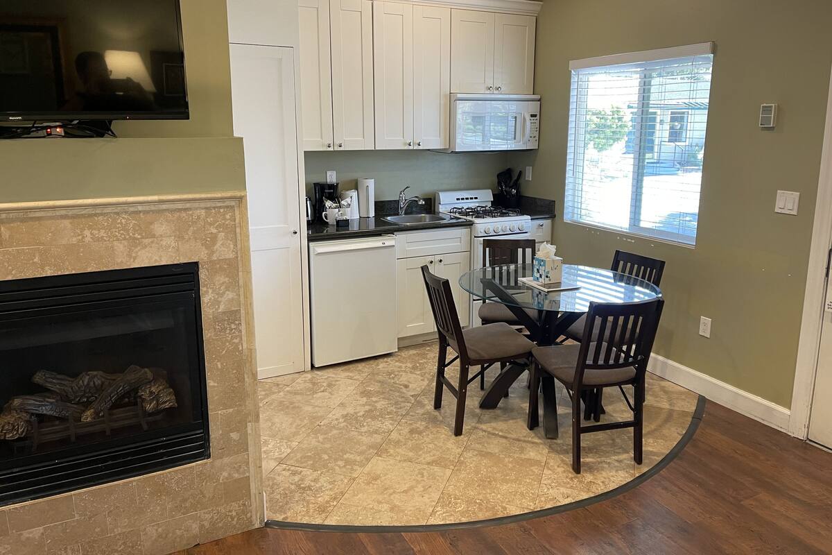 A modern kitchen with white cabinets, a gas stove, a microwave, and a dining area with a glass table and chairs.
