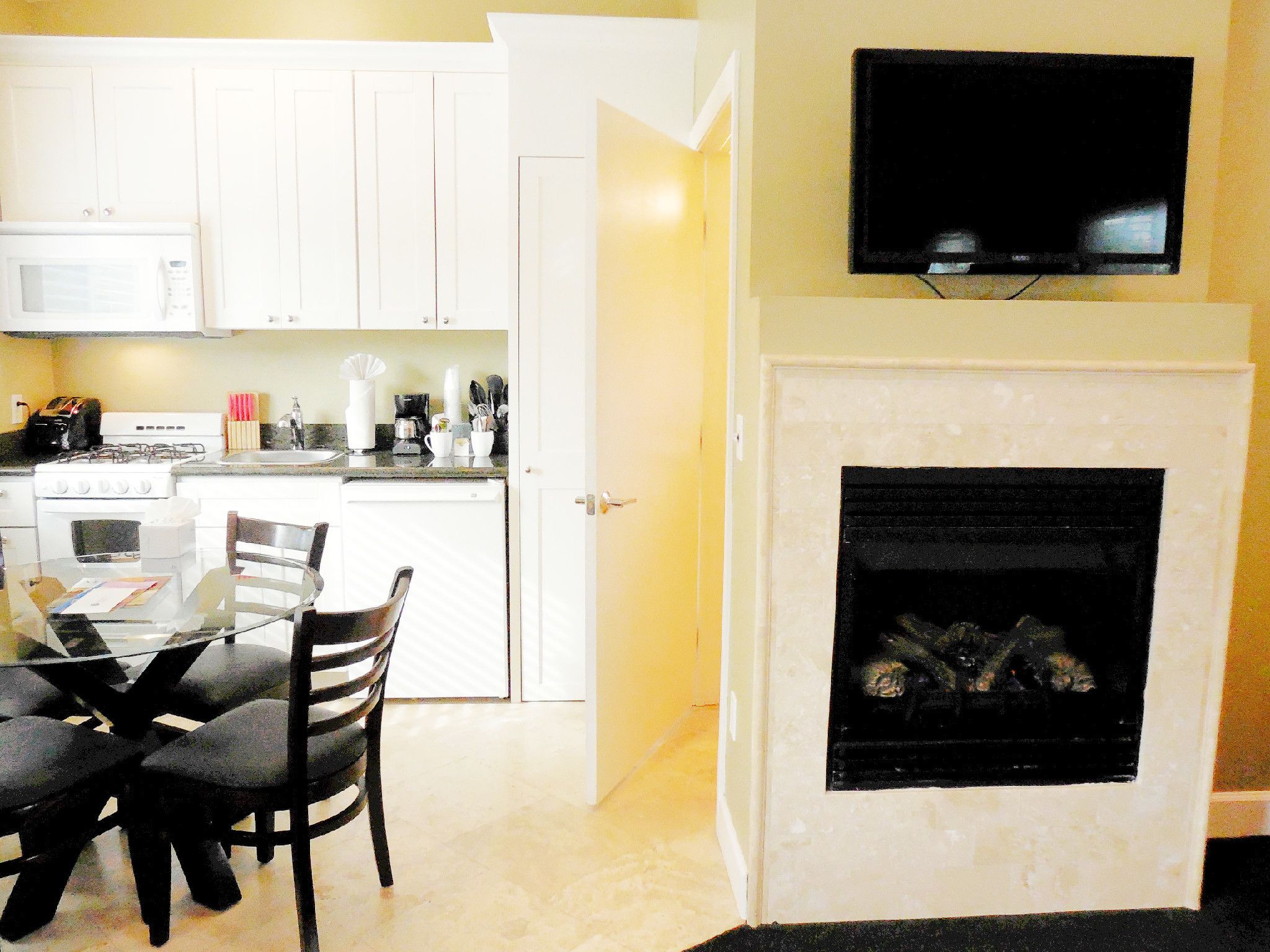 A compact kitchen with white cabinets, a microwave, a stove, and a dining area with a glass table and chairs.