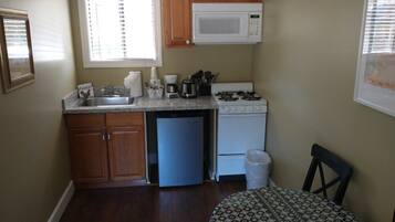A compact kitchen with wooden cabinets, a built-in microwave, a refrigerator, and a sink.