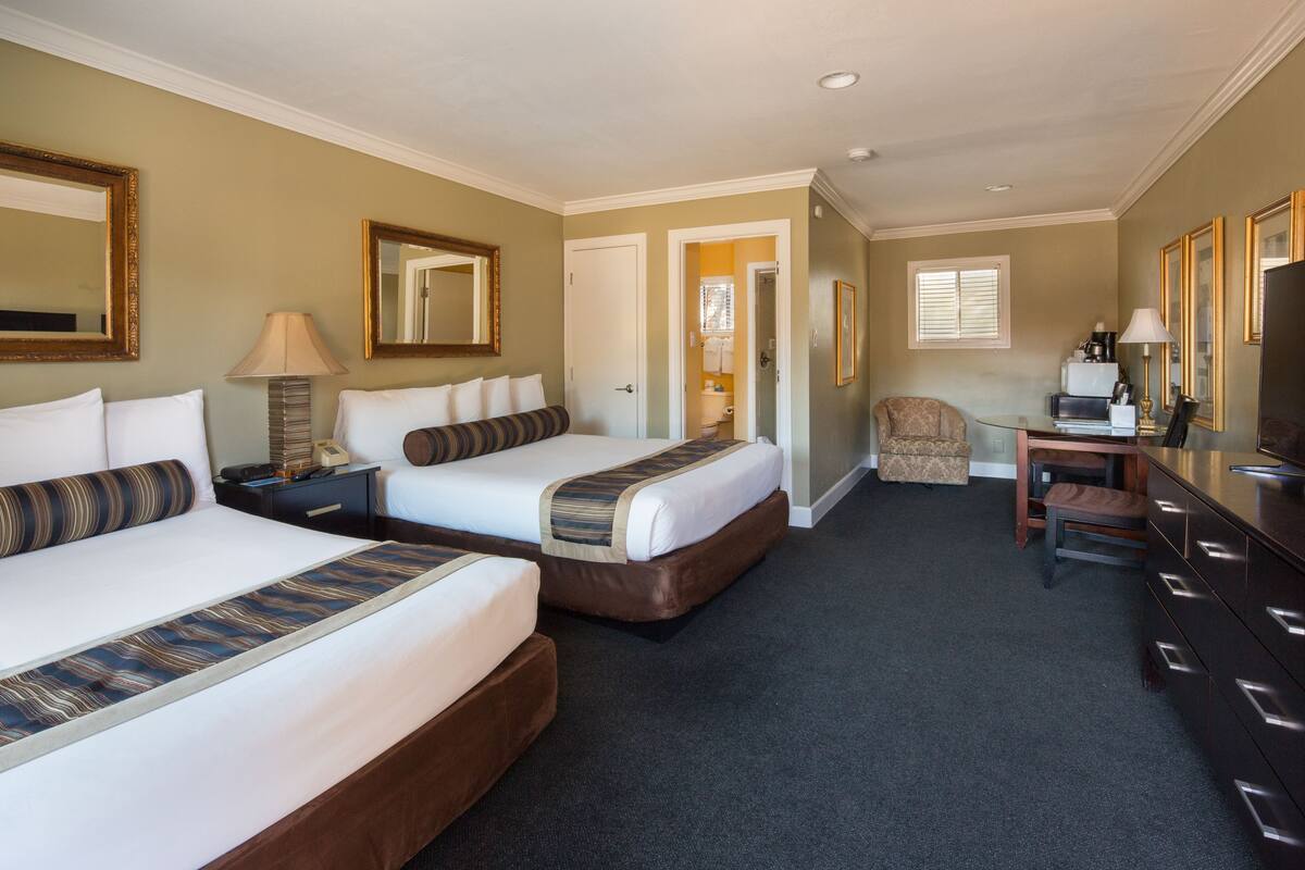 A hotel room with two beds, a desk, a chair, a television, and a mirror.