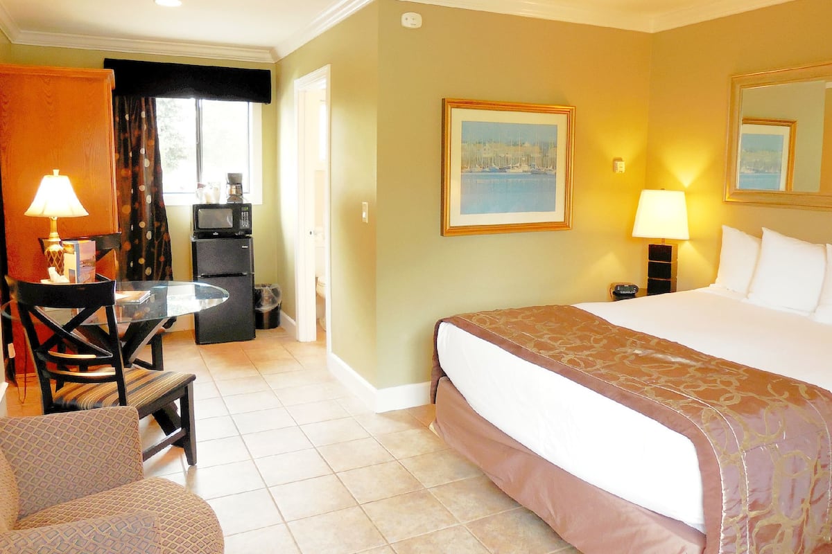 A hotel room with a bed, a desk with a lamp, a chair, a television, and a painting on the wall.
