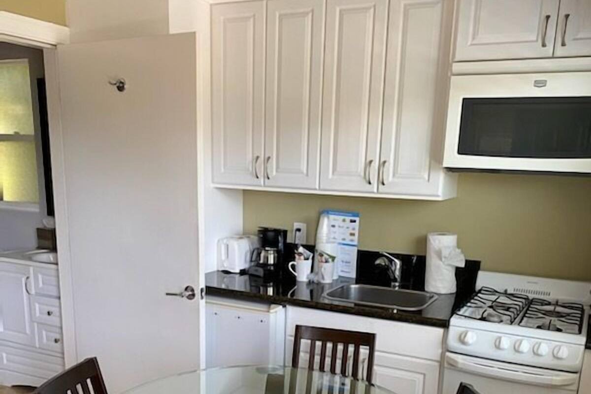 A compact kitchen with white cabinets, a glass-top dining table, and a stove.