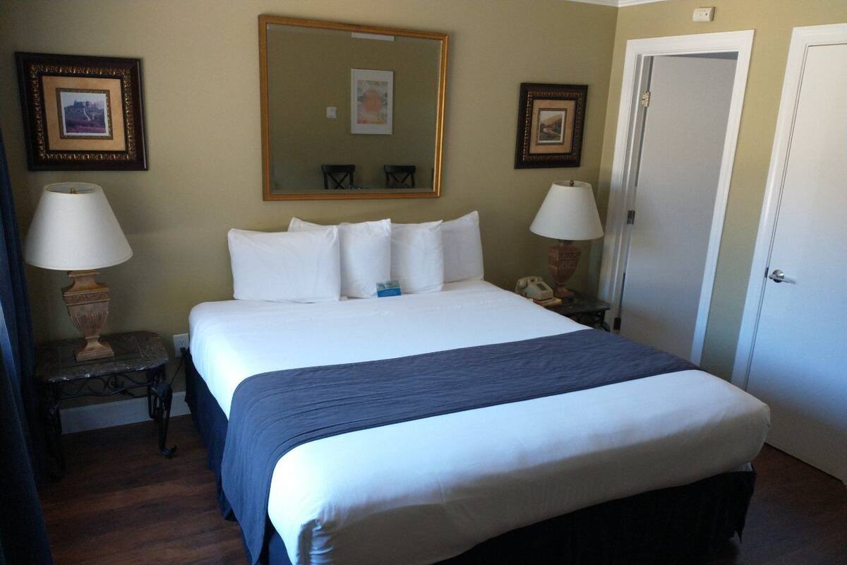 A hotel room with a large bed, two bedside tables, a nightstand, a mirror, and a door.