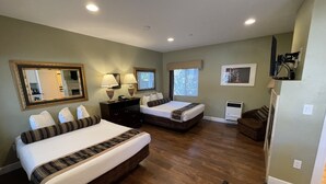 A hotel room with two beds, a desk, a chair, a mirror, a window, and a television.
