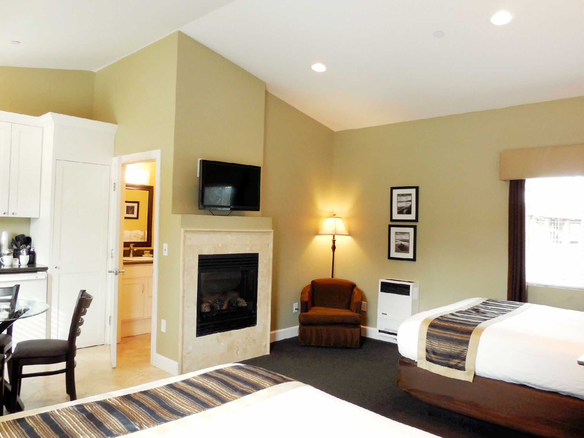 Una habitación de hotel con cama, chimenea, televisor, una silla y un escritorio con lámpara.