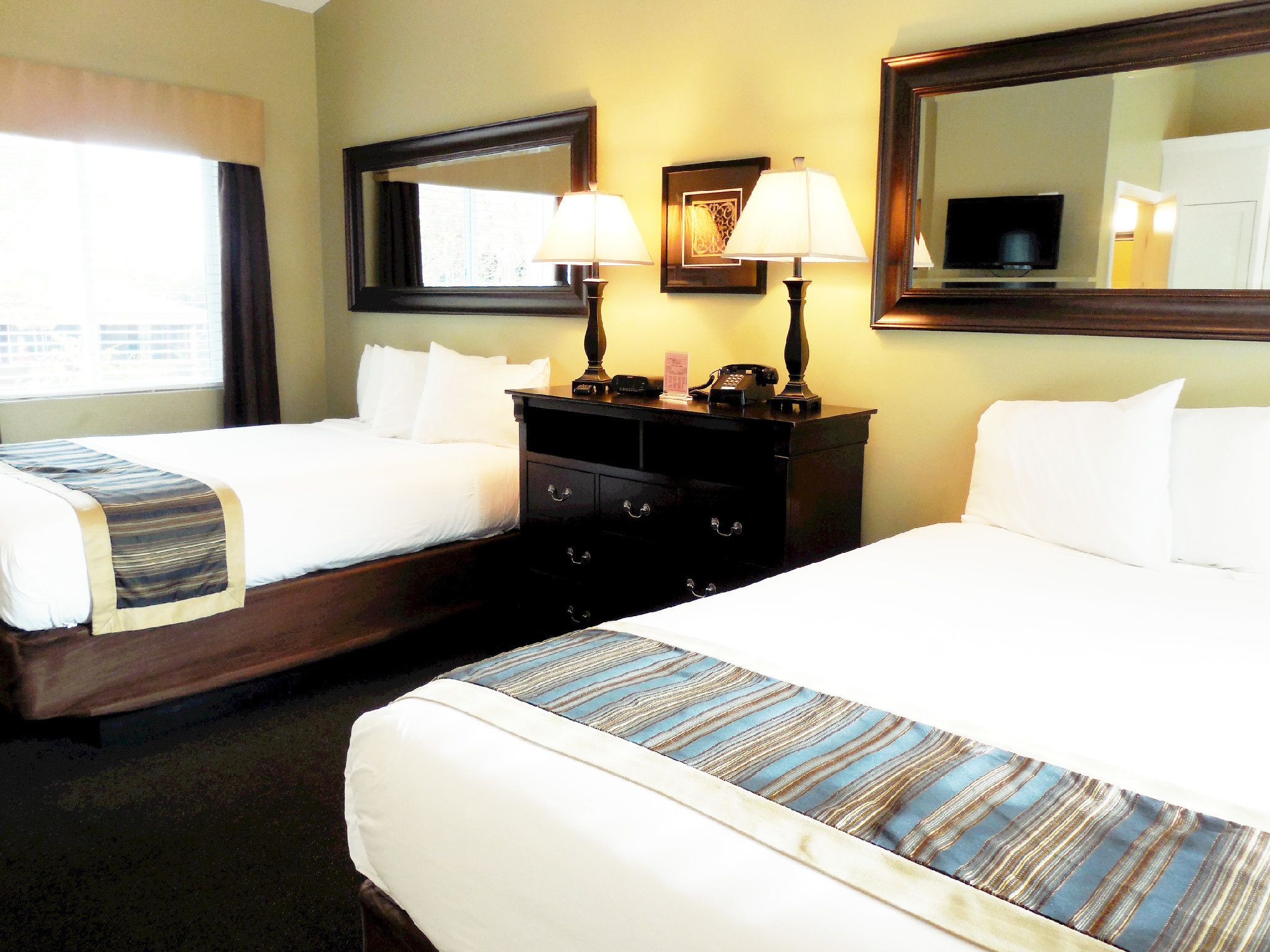 A hotel room with two beds, a dresser, a mirror, and a lamp.