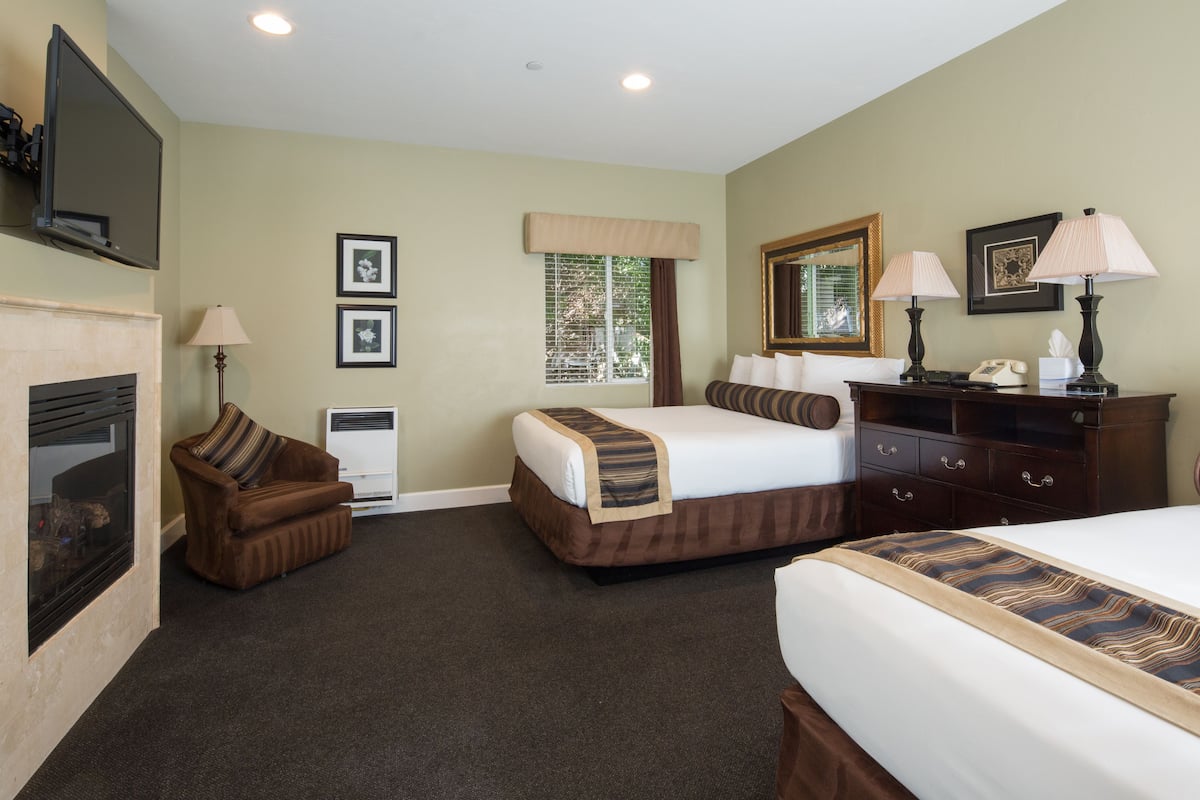 A hotel room with a bed, a sofa, a desk with a lamp, a fireplace, and framed pictures on the wall.