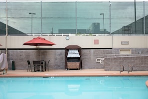 Un área de piscina con zona de estar cubierta, una parrilla y un letrero que indica los baños.