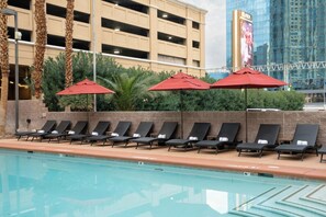 A poolside area with lounge chairs and red umbrellas, a spa pump sign, and a building with a large billboard in the background. - The Carriage House (Las Vegas)