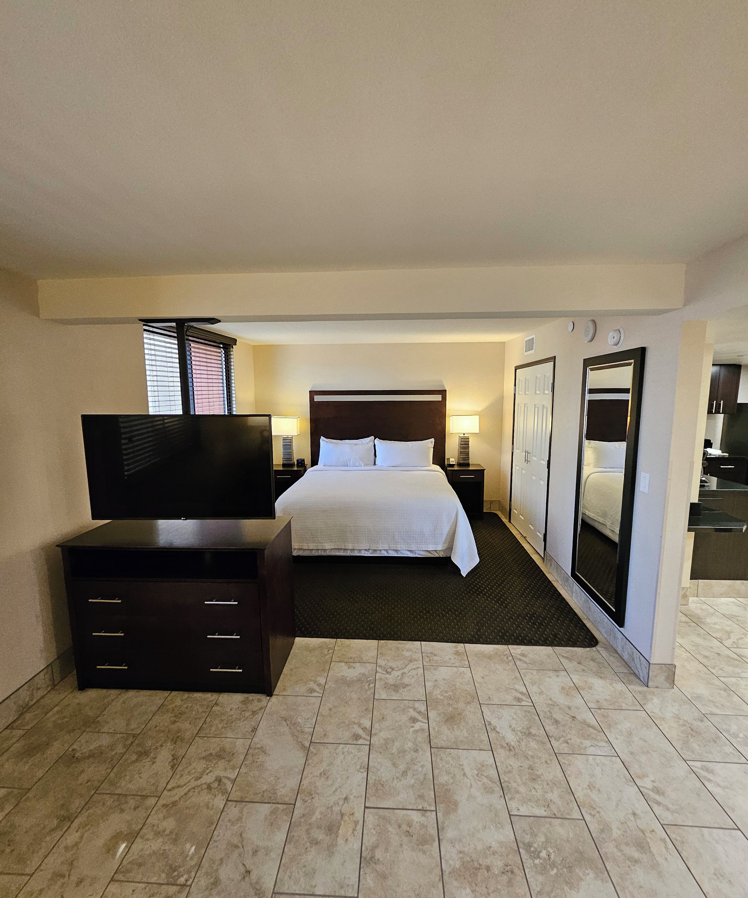 Een hotelkamer met een bed, een televisie, een dressoir, een spiegel en een kleine keukenhoek.