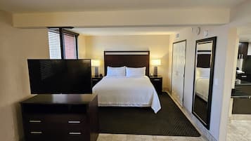 Een hotelkamer met een bed, een televisie, een dressoir, een spiegel en een kleine keukenhoek.