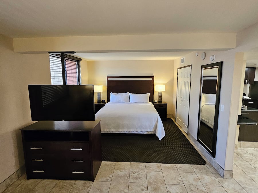 Een hotelkamer met een bed, een televisie, een dressoir, een spiegel en een kleine keukenhoek.