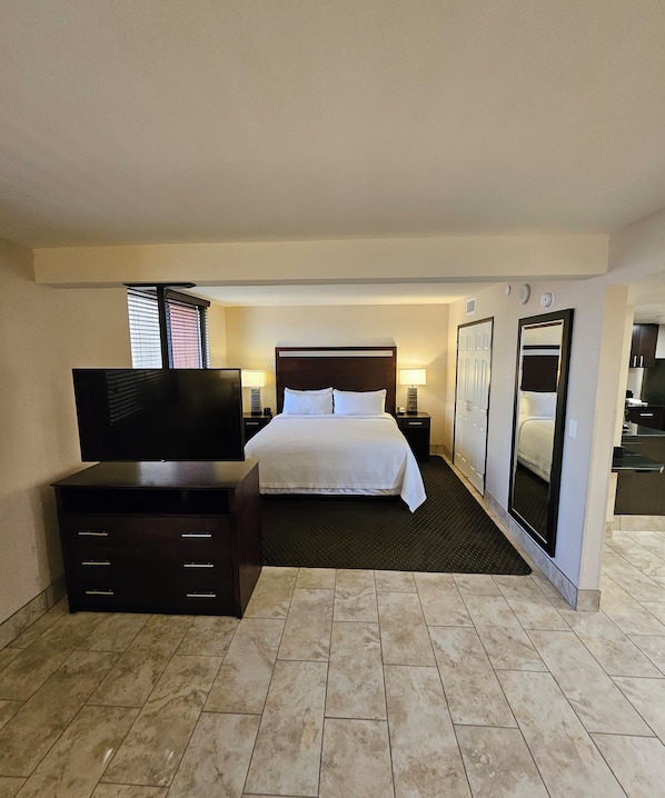 A hotel room with a bed, a TV, a dresser, a mirror, and a small kitchenette. - The Carriage House (Las Vegas)