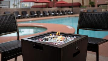 A poolside area with lounge chairs, a fire pit, and a pool.