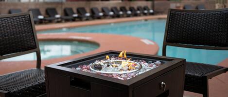 A poolside area with lounge chairs, a fire pit, and a pool.