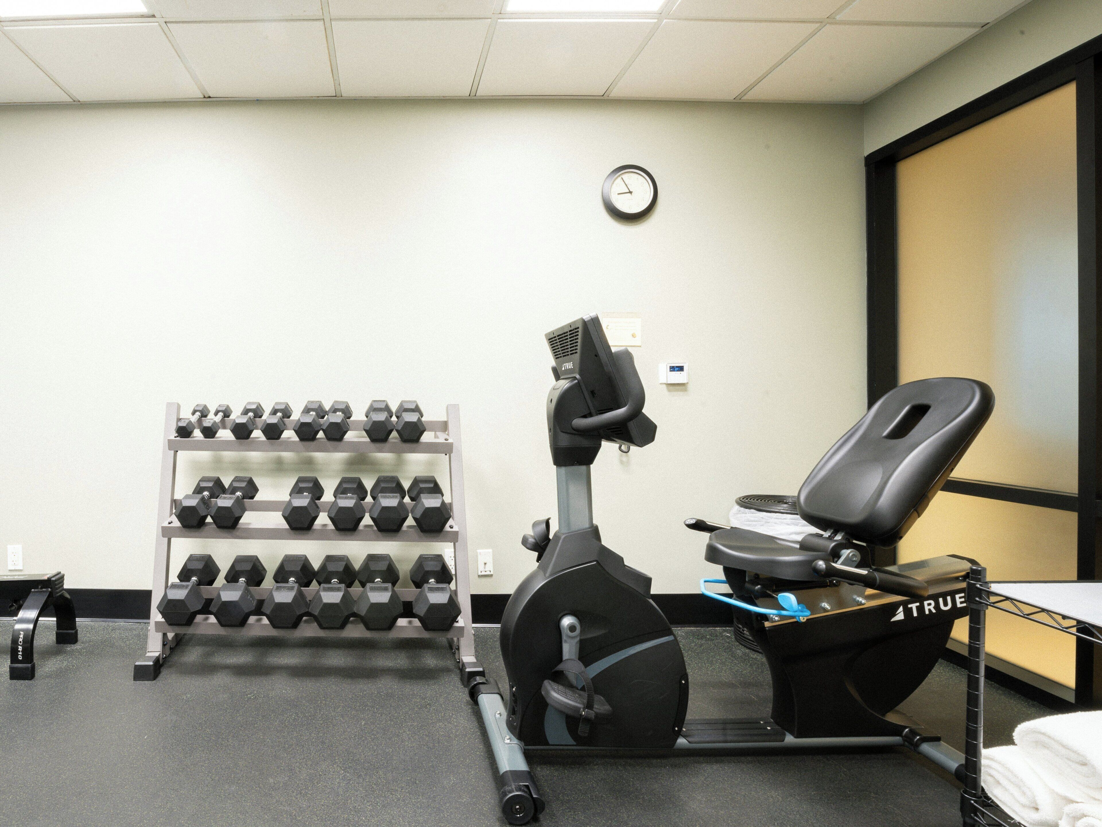 A gym with a treadmill, dumbbells, and a wall clock.