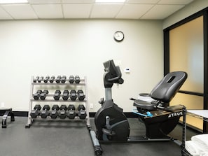 Un gimnasio con cinta de correr, mancuernas y un reloj de pared.