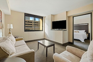 A hotel room with a sofa, a small table, a TV, and a bed. - The Carriage House (Las Vegas)
