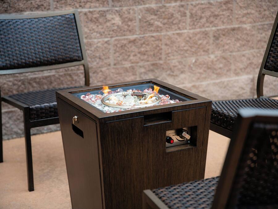 A portable outdoor grill with a metal grate and a control panel, placed on a wooden stand.
