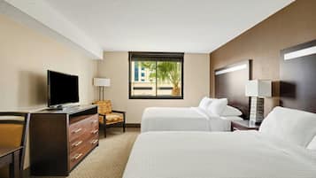 A hotel room with two beds, a desk, a TV, and a window with a view of palm trees.