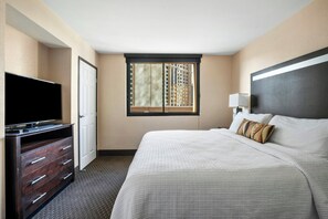Habitación de hotel con cama, televisión, cómoda y ventana con persianas.