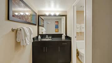A bathroom with a dark vanity, a sink, and a mirror. There are towels hanging on the wall and a toilet visible in the background.