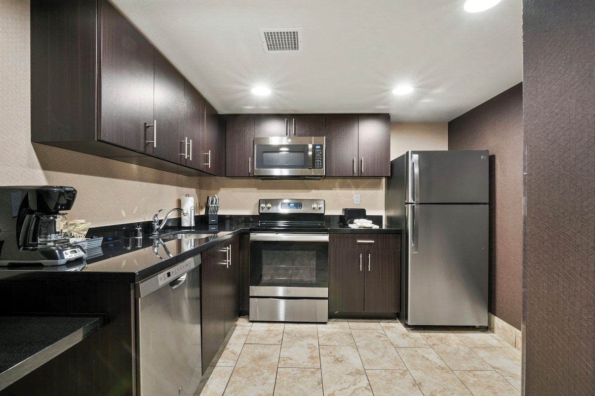 A modern kitchen with stainless steel appliances, dark cabinetry, and a tiled floor.