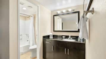 Un baño con bañera, inodoro y tocador con espejo y lavamanos.