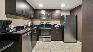 A modern kitchen with stainless steel appliances, dark cabinetry, and a tiled floor. - The Carriage House (Las Vegas)