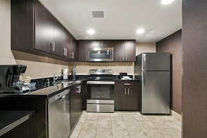 A modern kitchen with stainless steel appliances, dark cabinetry, and a tiled floor. - The Carriage House (Las Vegas)