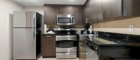 A modern kitchen with stainless steel appliances, dark wood cabinets, and a black granite countertop.