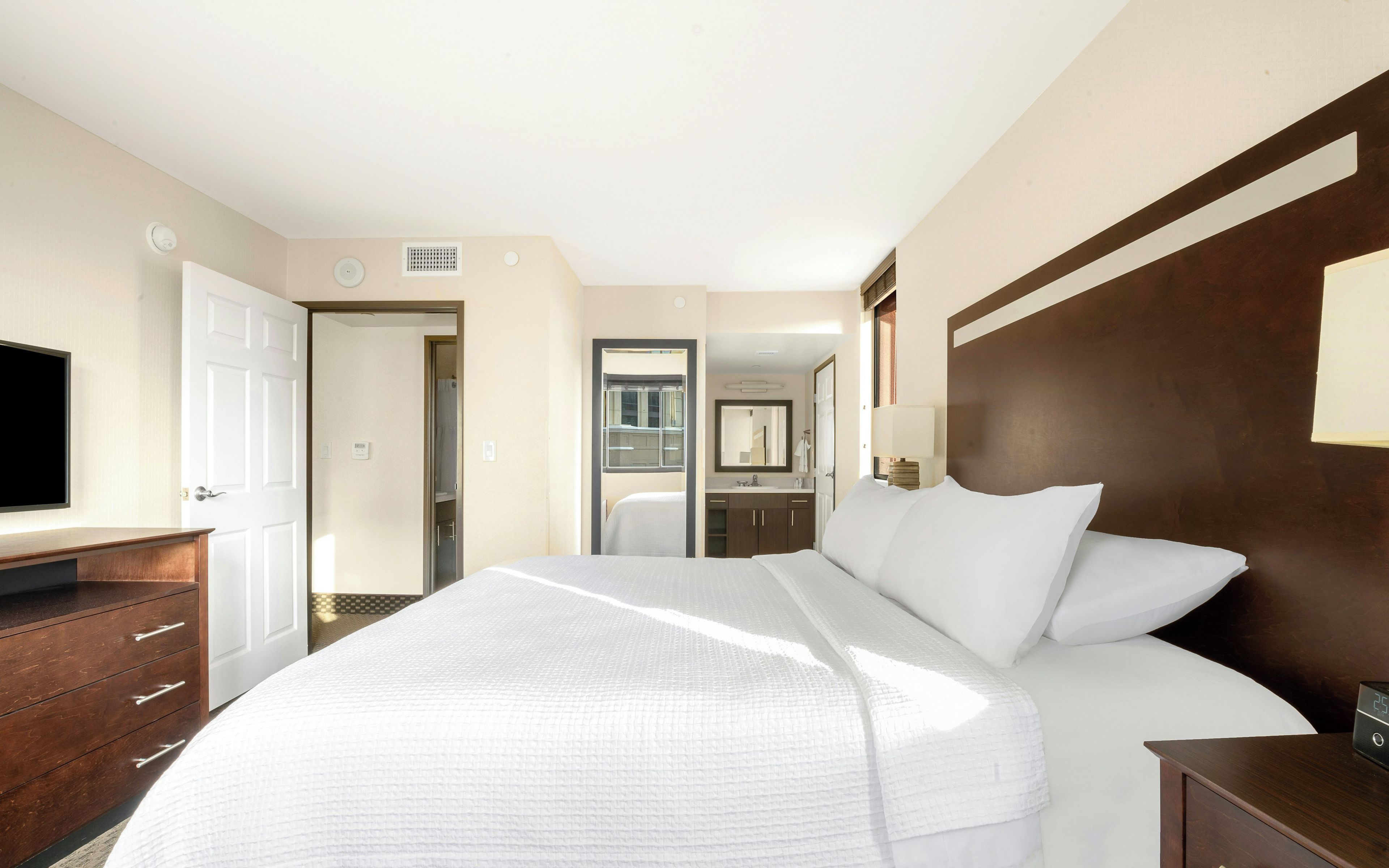 Ein Hotelzimmer mit einem großen Bett, einem Fernseher, einem Schreibtisch und einem Kleiderschrank.