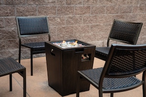 A square outdoor seating area with a built-in fire feature, surrounded by chairs with woven backs. - The Carriage House (Las Vegas)
