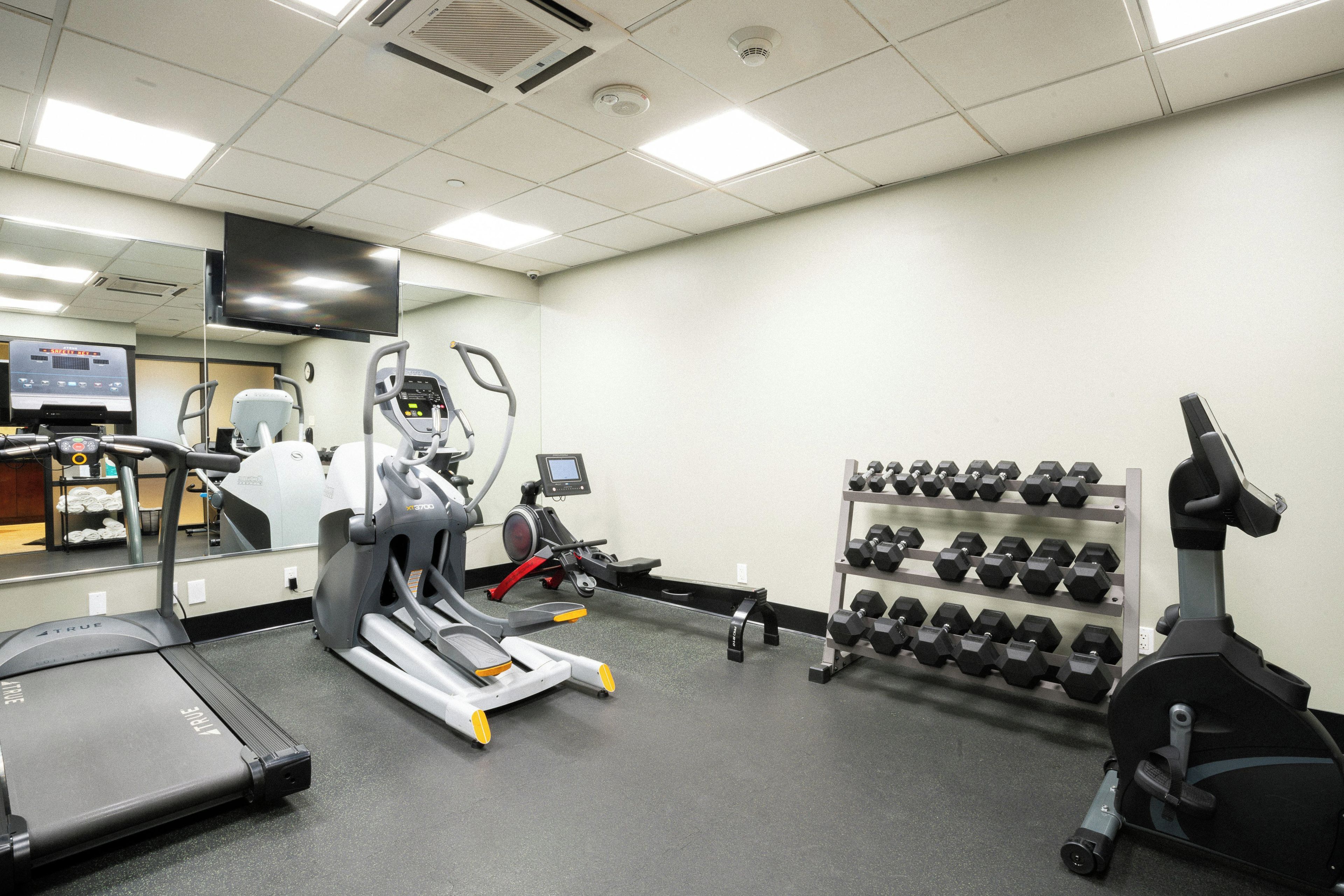 Une salle de sport équipée de divers appareils, notamment des tapis de course, un vélo elliptique et un porte-haltères.