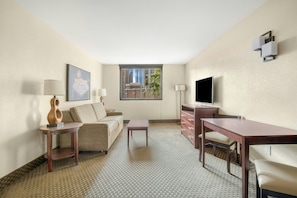 Habitación de hotel con sofá, una mesita, escritorio, televisor y ventana con vista a edificios.