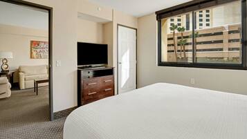 A hotel room with a bed, a dresser, a television, and a window with a view of a building and palm trees.