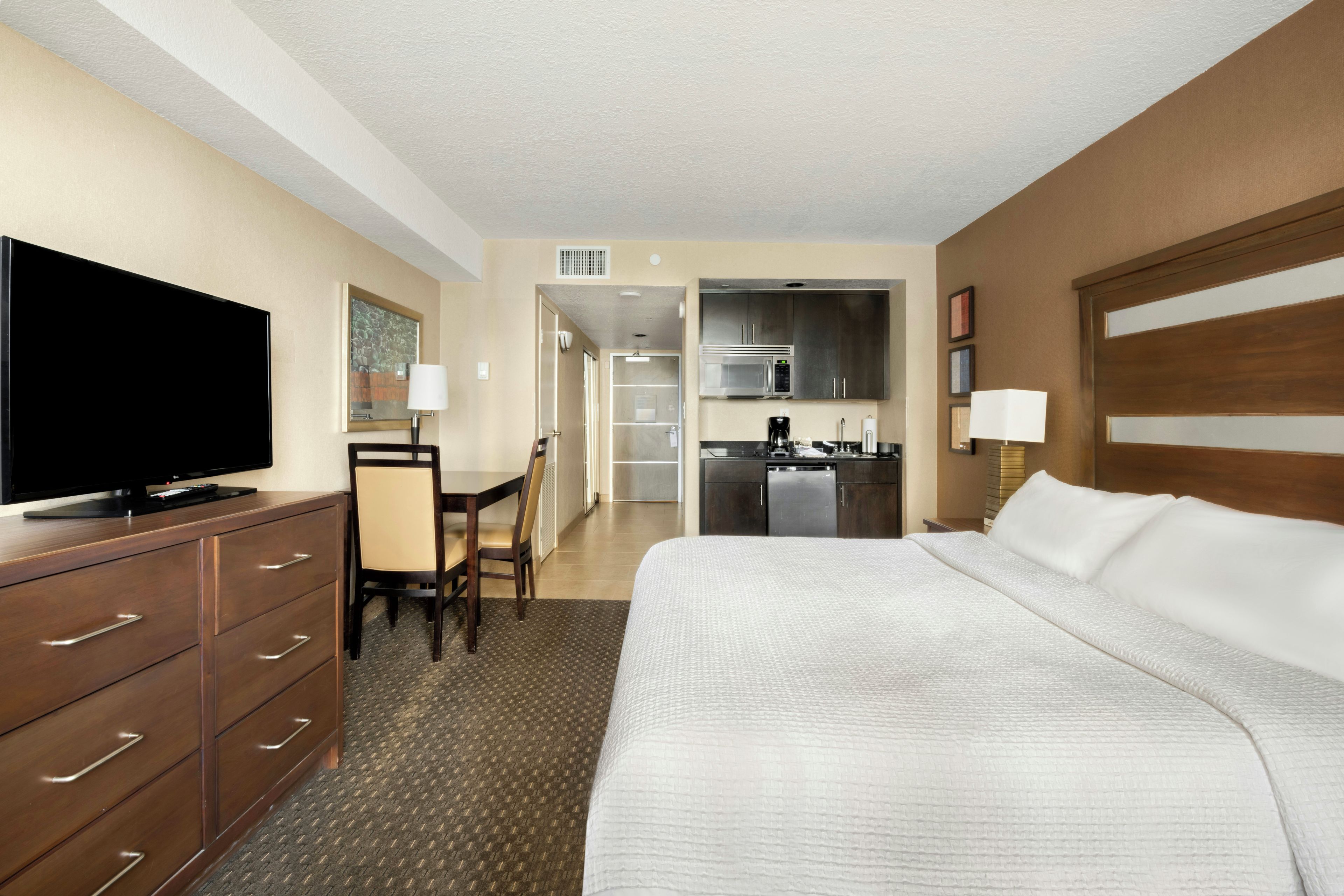 Ein Hotelzimmer mit Bett, Fernseher, Schreibtisch mit Stuhl, einer Küchenzeile und einem Badezimmer.