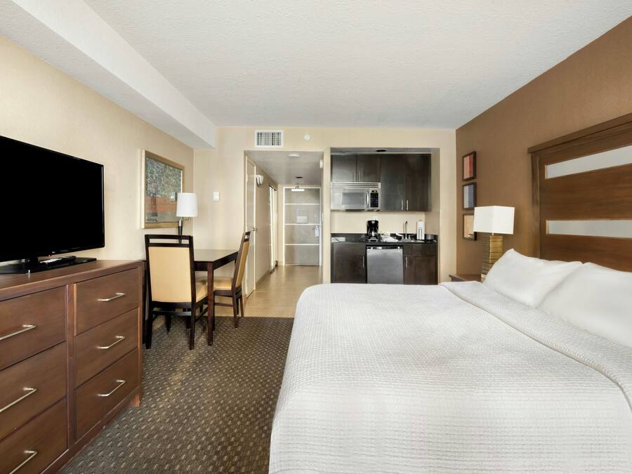 Ein Hotelzimmer mit Bett, Fernseher, Schreibtisch mit Stuhl, einer Küchenzeile und einem Badezimmer.