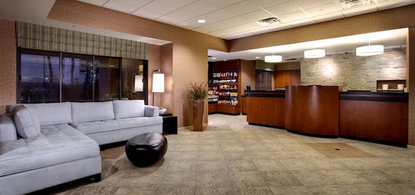 A hotel lobby with a reception desk, a seating area with a sofa, and a small round table. - The Carriage House (Las Vegas)