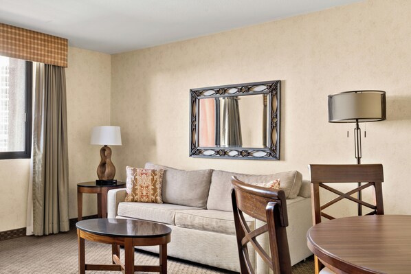 A hotel room with a sofa, a round table, a lamp, and a mirror on the wall. - The Carriage House (Las Vegas)