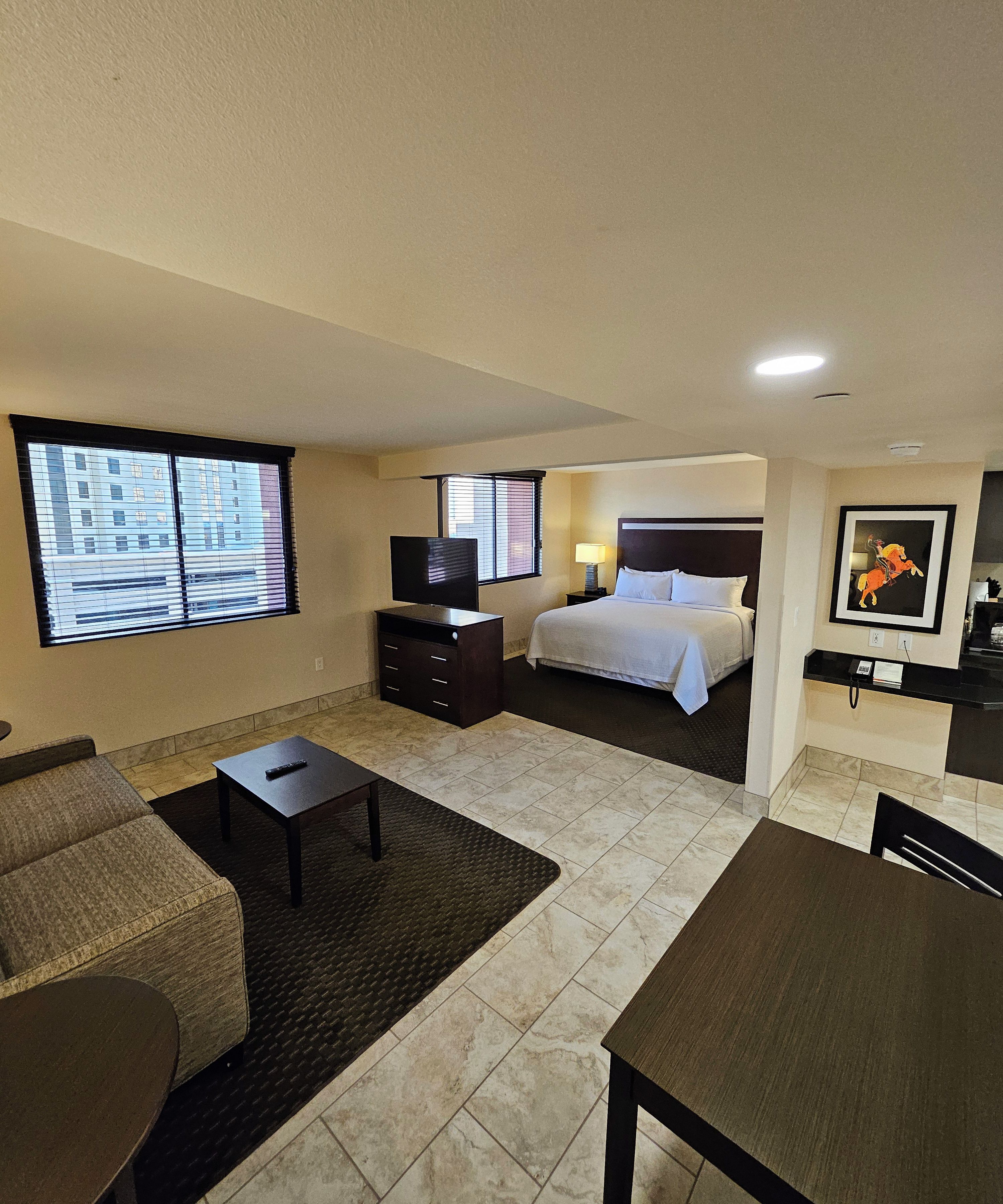 Une chambre d’hôtel équipée d’un lit, d’une télévision, d’un bureau, d’une chaise, d’un canapé et d’une fenêtre avec des stores.