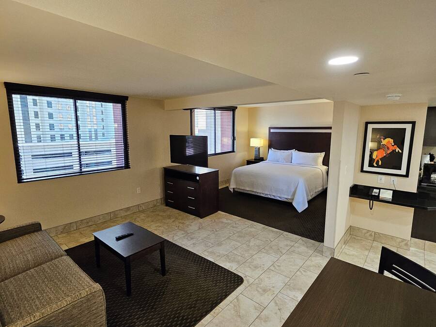Une chambre d’hôtel équipée d’un lit, d’une télévision, d’un bureau, d’une chaise, d’un canapé et d’une fenêtre avec des stores.