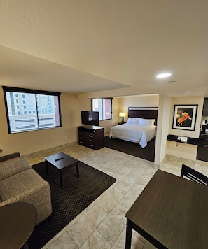 A hotel room with a bed, a TV, a desk, a chair, a sofa, and a window with blinds. - The Carriage House (Las Vegas)