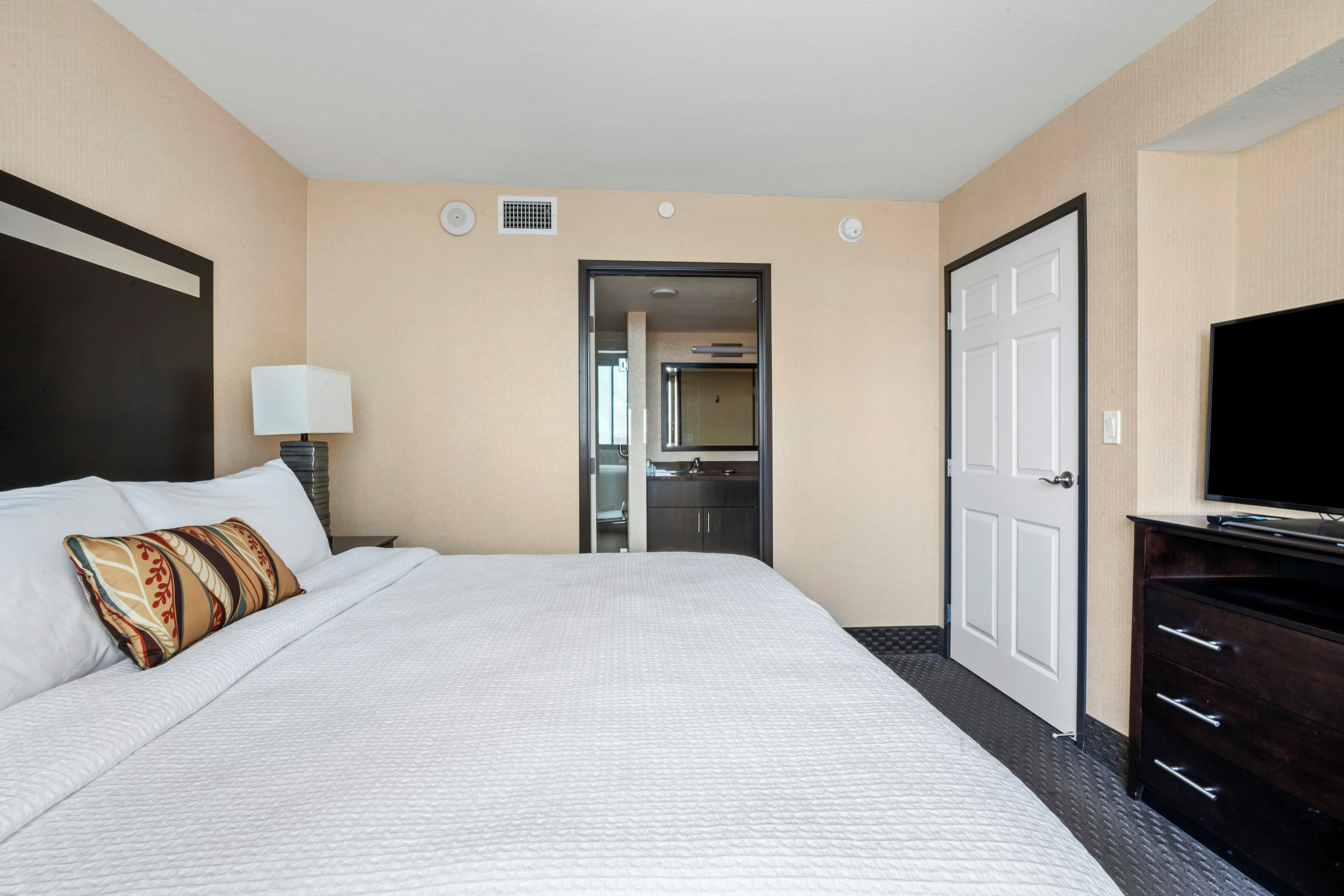 A hotel room with a large bed, a television, a desk, and a bathroom visible through an open door.