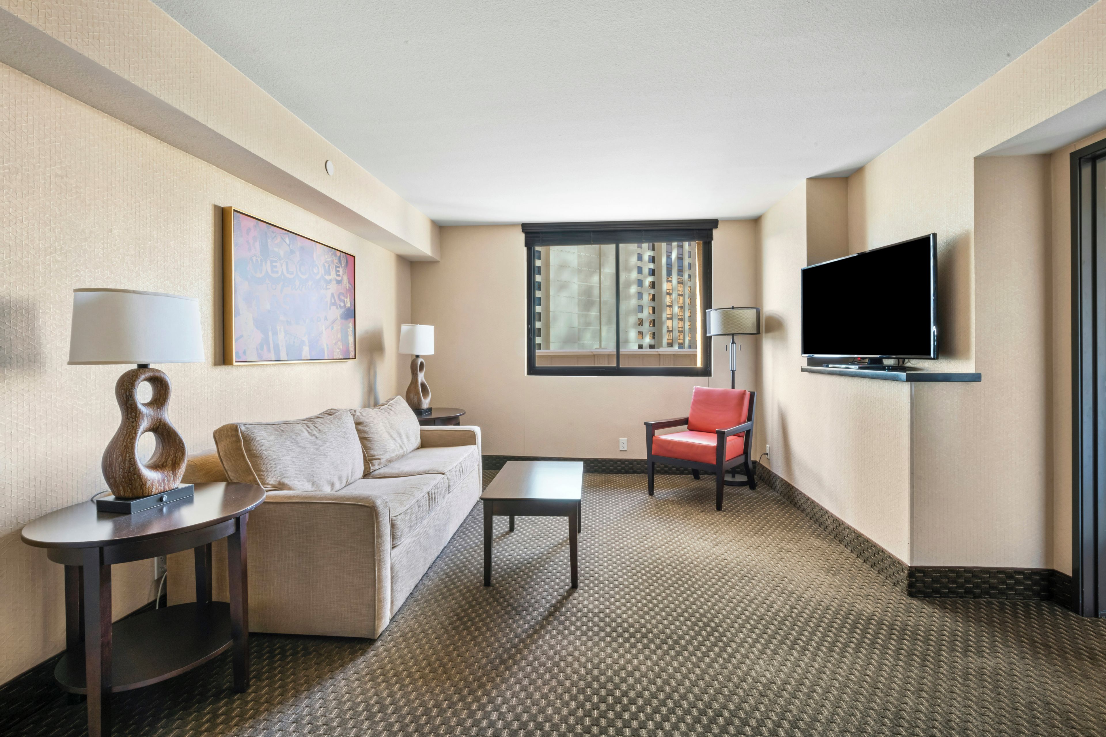 Een hotelkamer met een bank, een stoel, een salontafel, een televisie en een raam met zonwering.