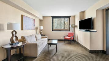 Een hotelkamer met een bank, een stoel, een salontafel, een televisie en een raam met zonwering.
