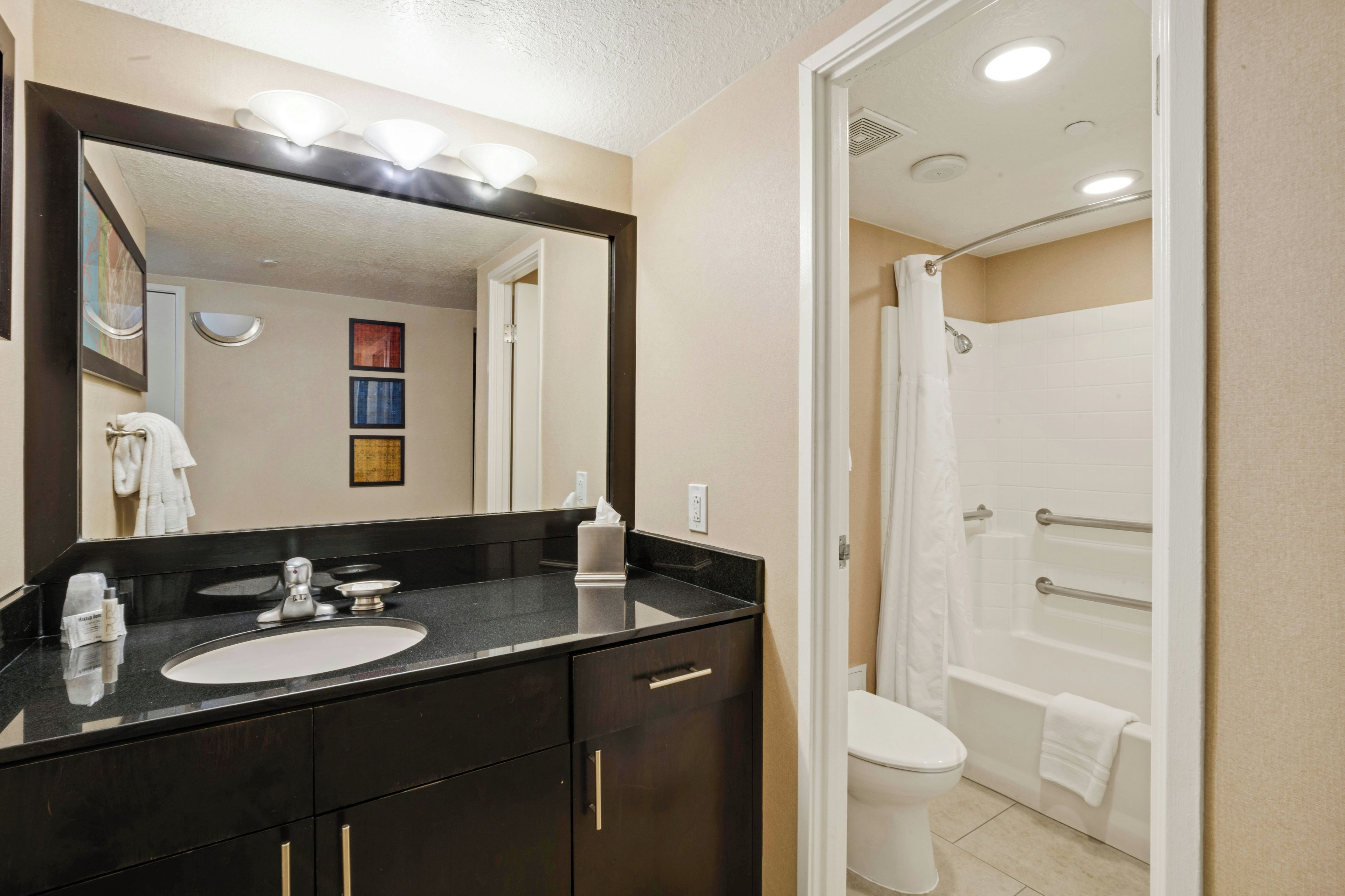 Une salle de bain d’hôtel équipée d’un lavabo, d’un miroir, d’un porte-serviettes et d’un espace douche.