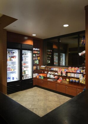 A small, well-lit convenience store with refrigerated sections on the left, shelves stocked with snacks and beverages, and a counter with various products. - The Carriage House (Las Vegas)